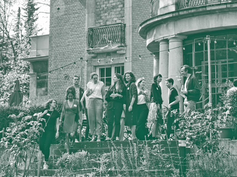 Eine Gruppe von Menschen steht vor einer alten Villa und führt Gespräche.